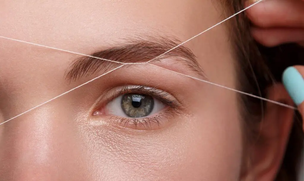 Beautiful woman doing eyebrow correction with a white thread